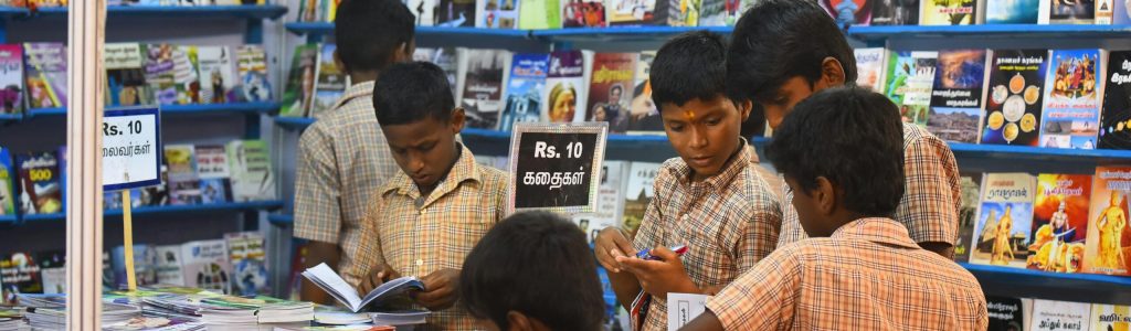 Children engaged in browsing books at a stall in Madurai, highlighting interest in reading and education.