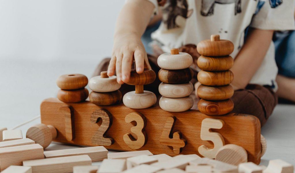 Child's hand interacting with wooden educational toys and number blocks indoors.